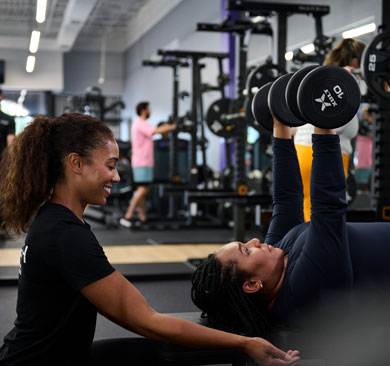 Personal trainer coaching a client through a supervised dumbbell chest press in a modern gym setting, emphasizing safe strength training and proper form.