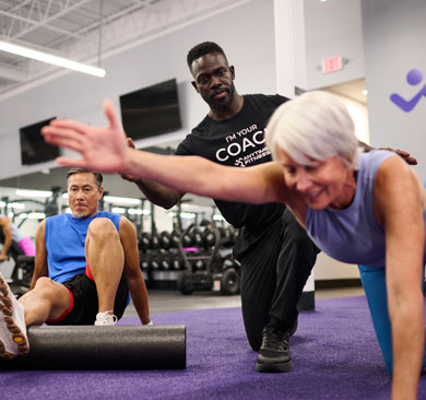 Coach guiding older adults through a supervised small group strength and mobility exercise session in a modern gym setting.